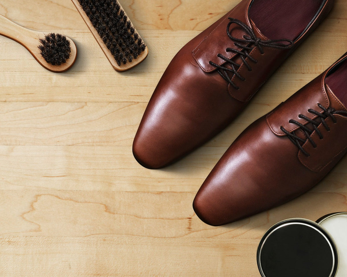 Polished brown leather dress shoes with shoe care brushes and polish on wooden surface