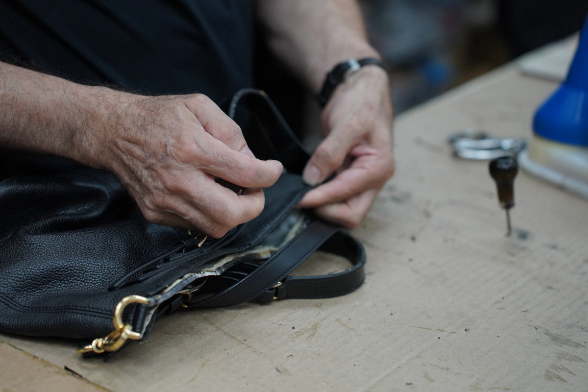 ShoeMedic artisan repairing the zipper and stitching of a black leather handbag